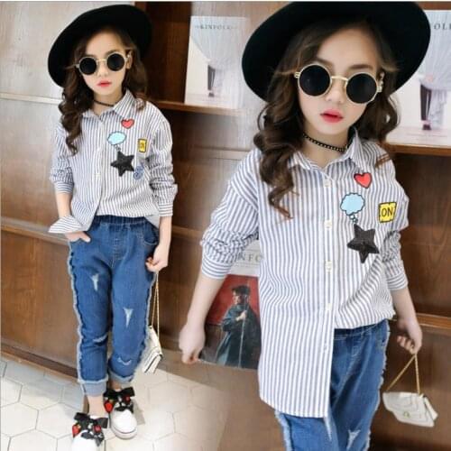 The little girl wears a fashionable long-sleeved striped shirt with a black star and a heart pattern