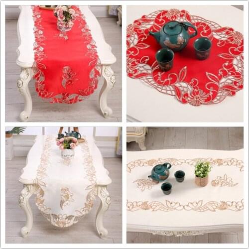 The new red embroidered table runner. Openwork lace tablecloth. The oval coffee table is covered with cloth. Beige table cloth